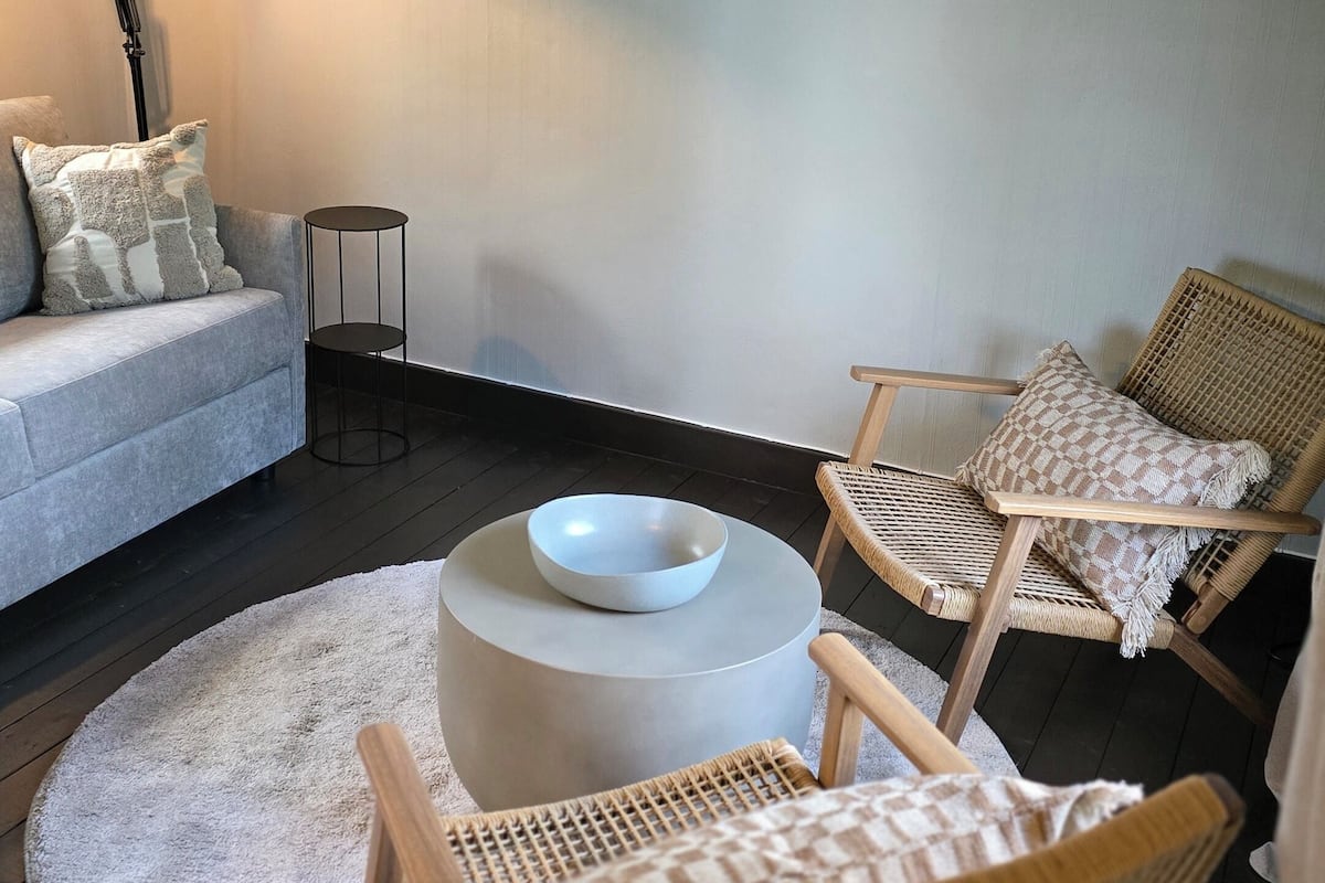 A room with a round table, two wicker chairs, a sofa, a floor lamp, and a small side table.