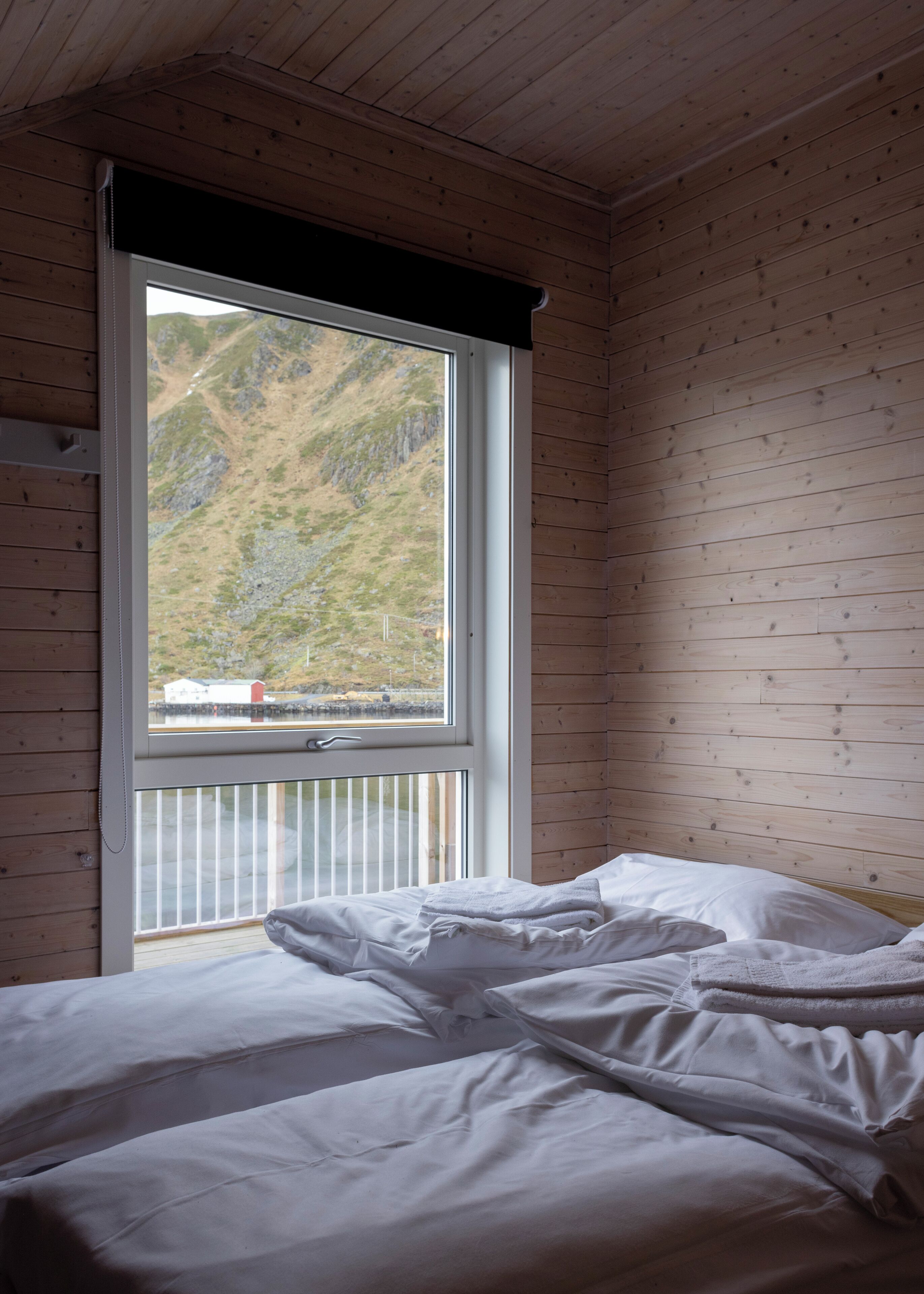 A bedroom with a large window, wooden walls, and a bed with white bedding.