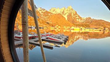 Ein rundes Fenster mit Blick auf einen stillen See, Boote und Berge.