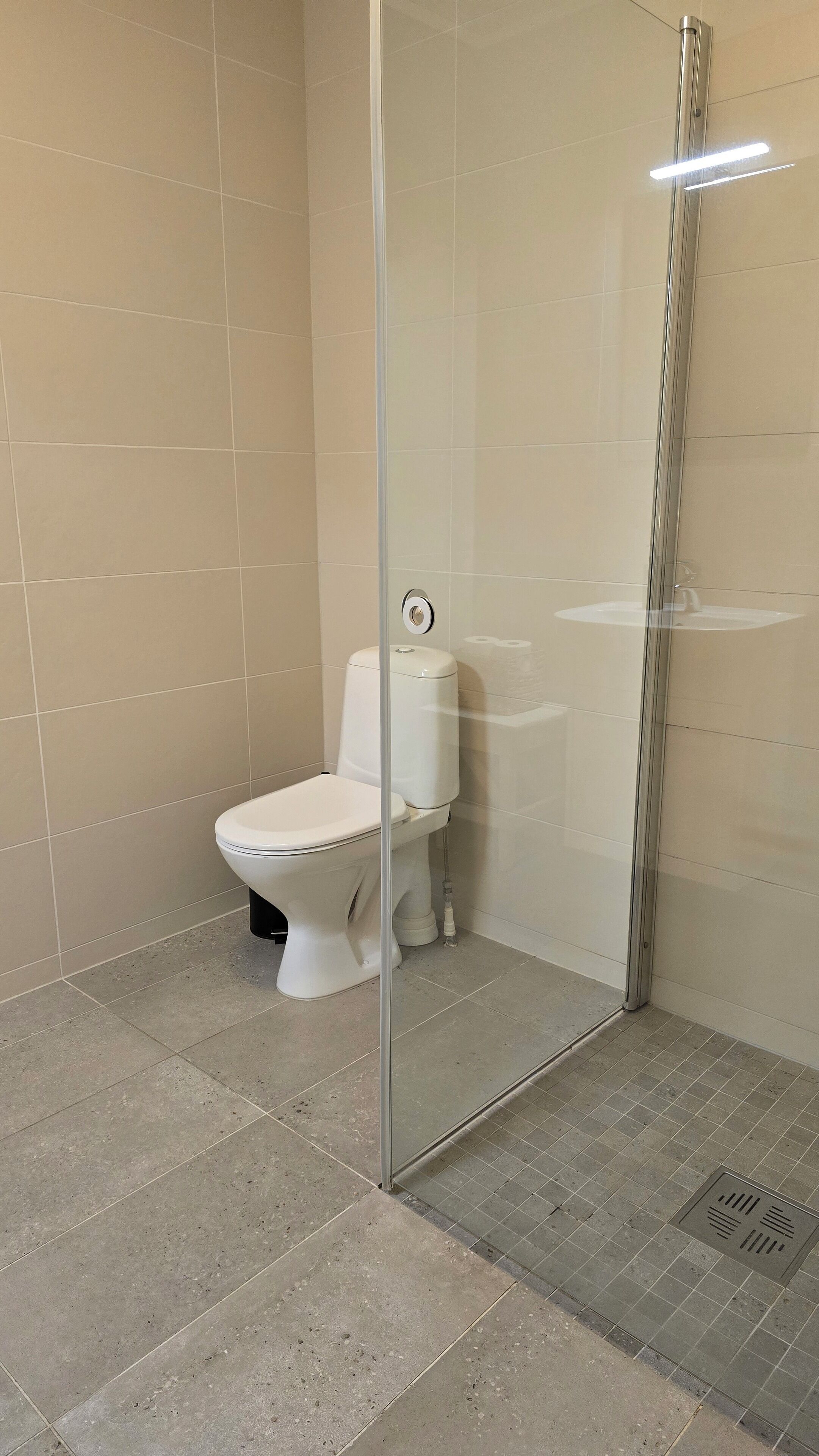 Un baño con inodoro, cabina de ducha de vidrio y paredes de azulejos.