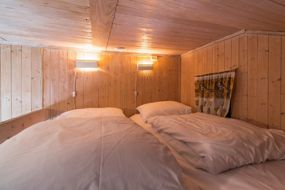 A room with wooden walls, two beds with white bedding, and two wall-mounted lights.