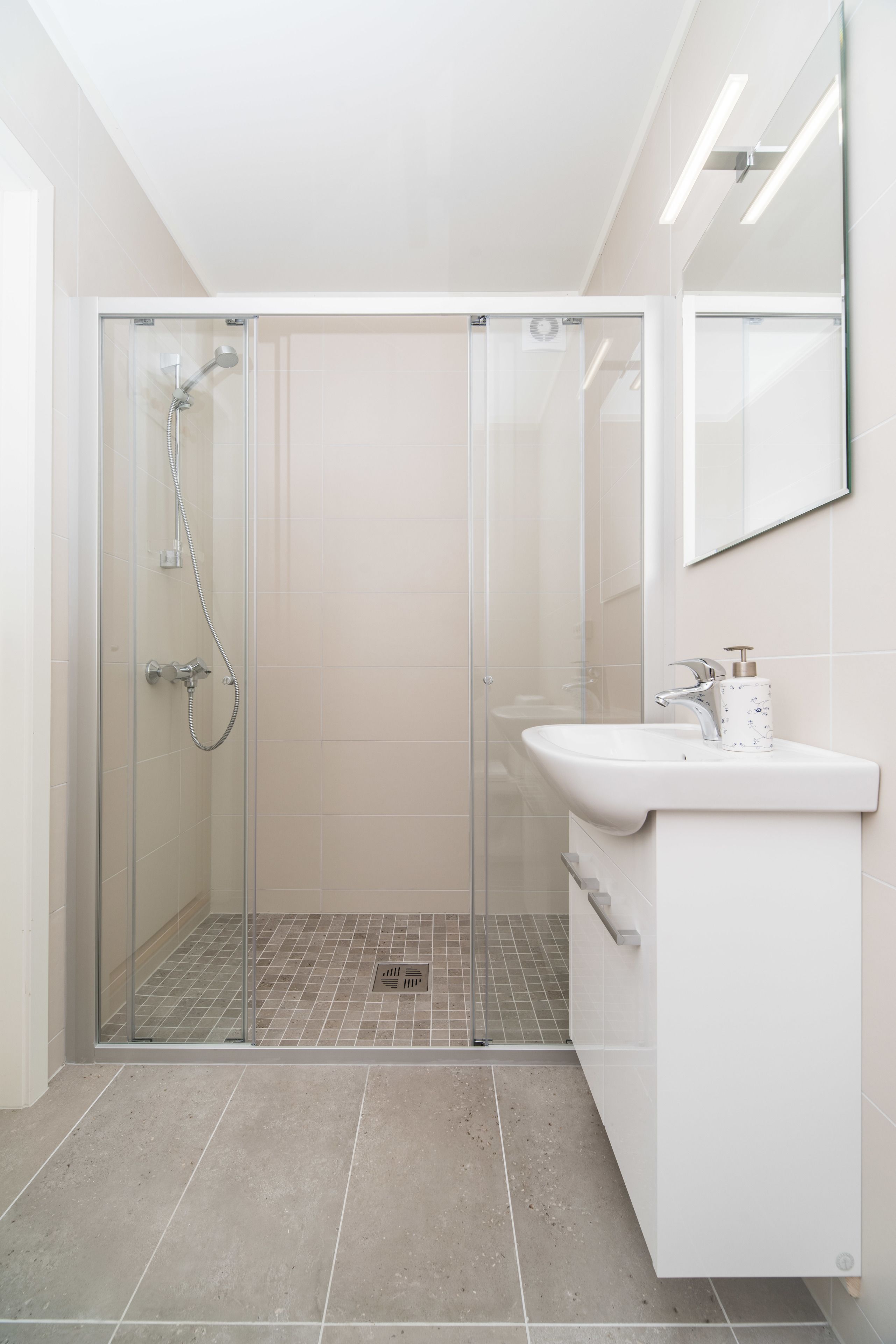 A modern bathroom with a glass-enclosed shower, a white sink, and a mirror above it.