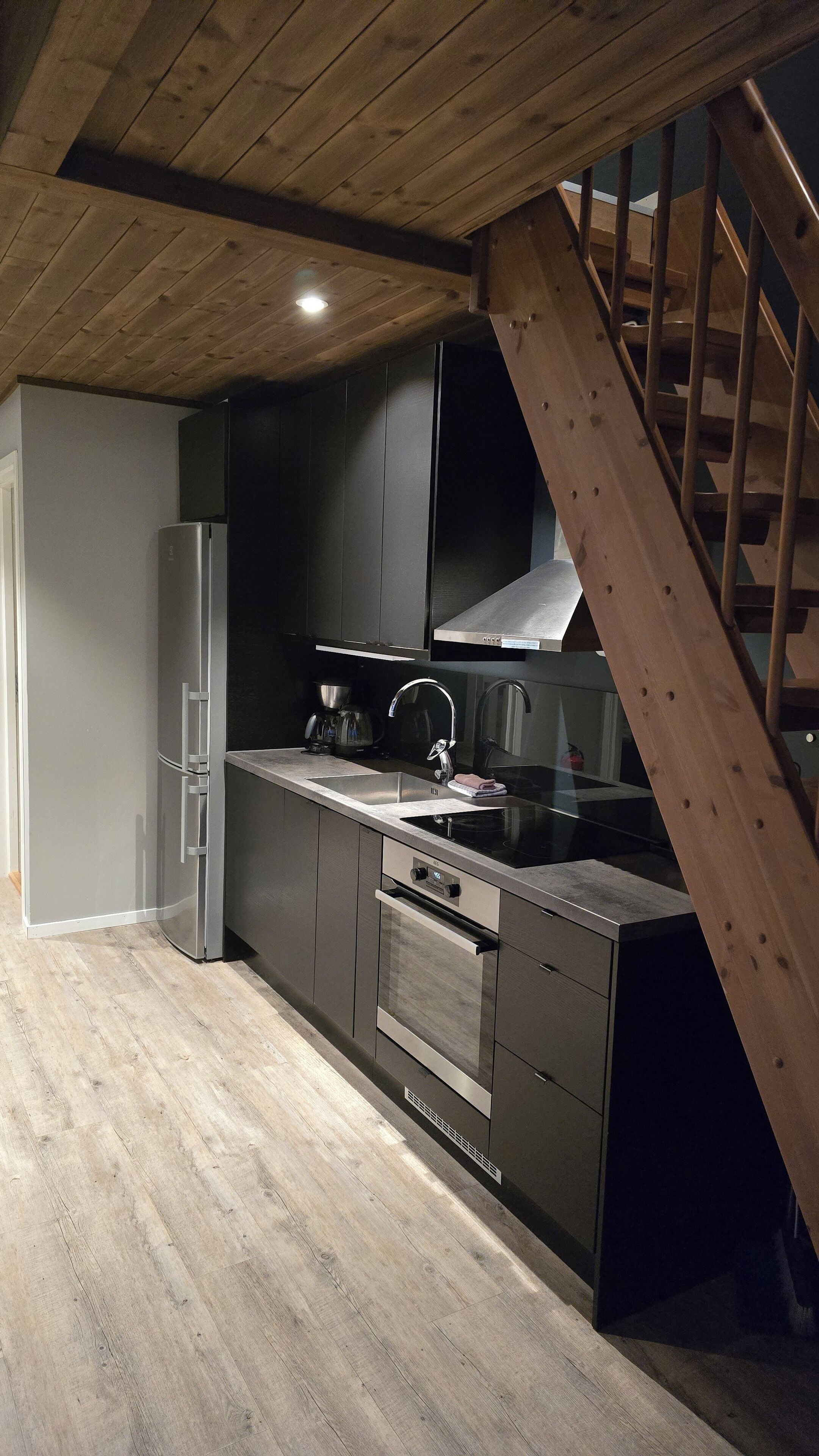 A modern kitchen with stainless steel appliances, a wooden staircase, and a dark-colored cabinet.