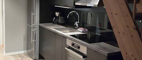 A modern kitchen with stainless steel appliances, a wooden staircase, and a dark-colored cabinet.
