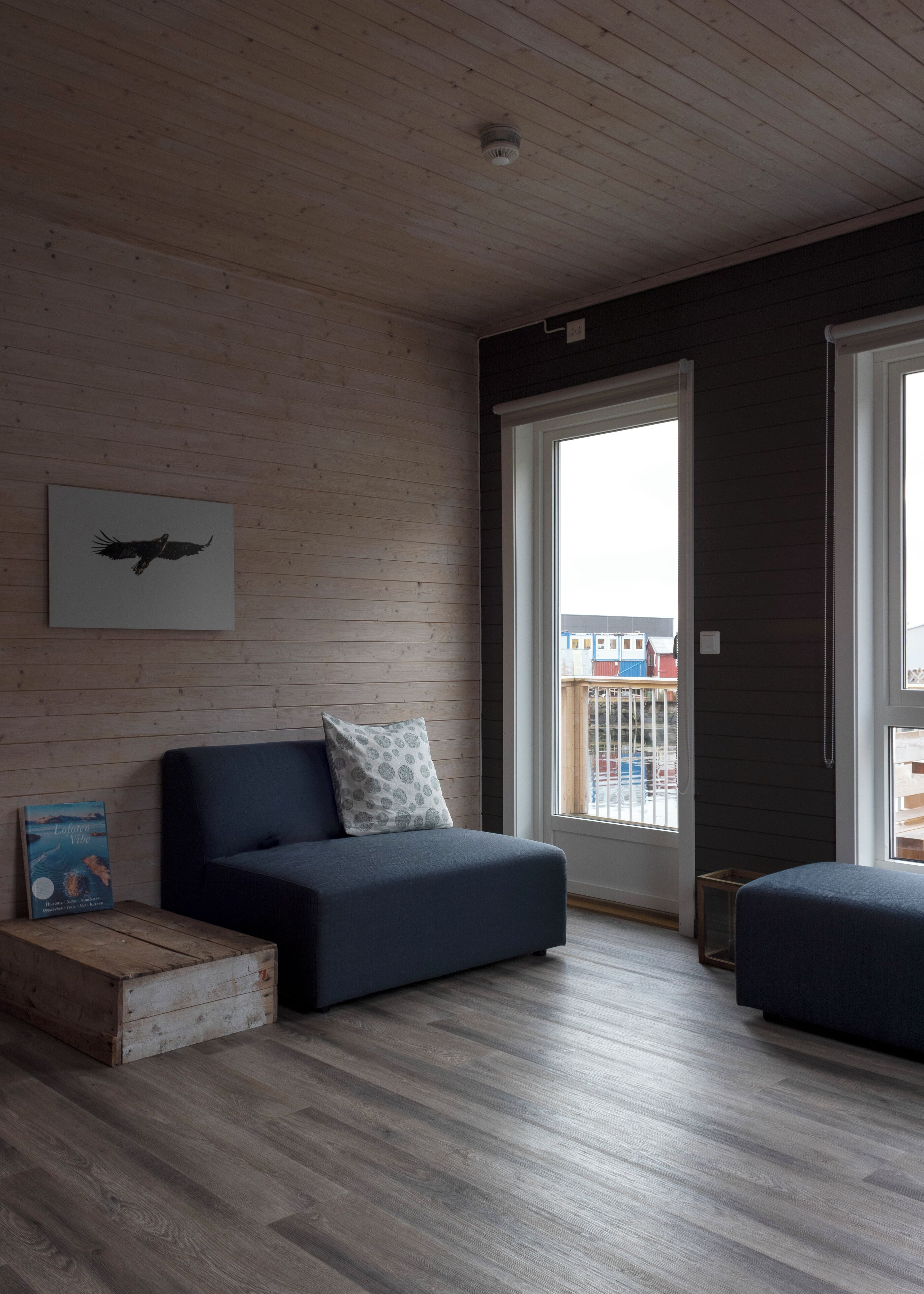Un salon moderne avec un canapé bleu foncé, une table basse en bois et une œuvre d’art encadrée représentant un oiseau.