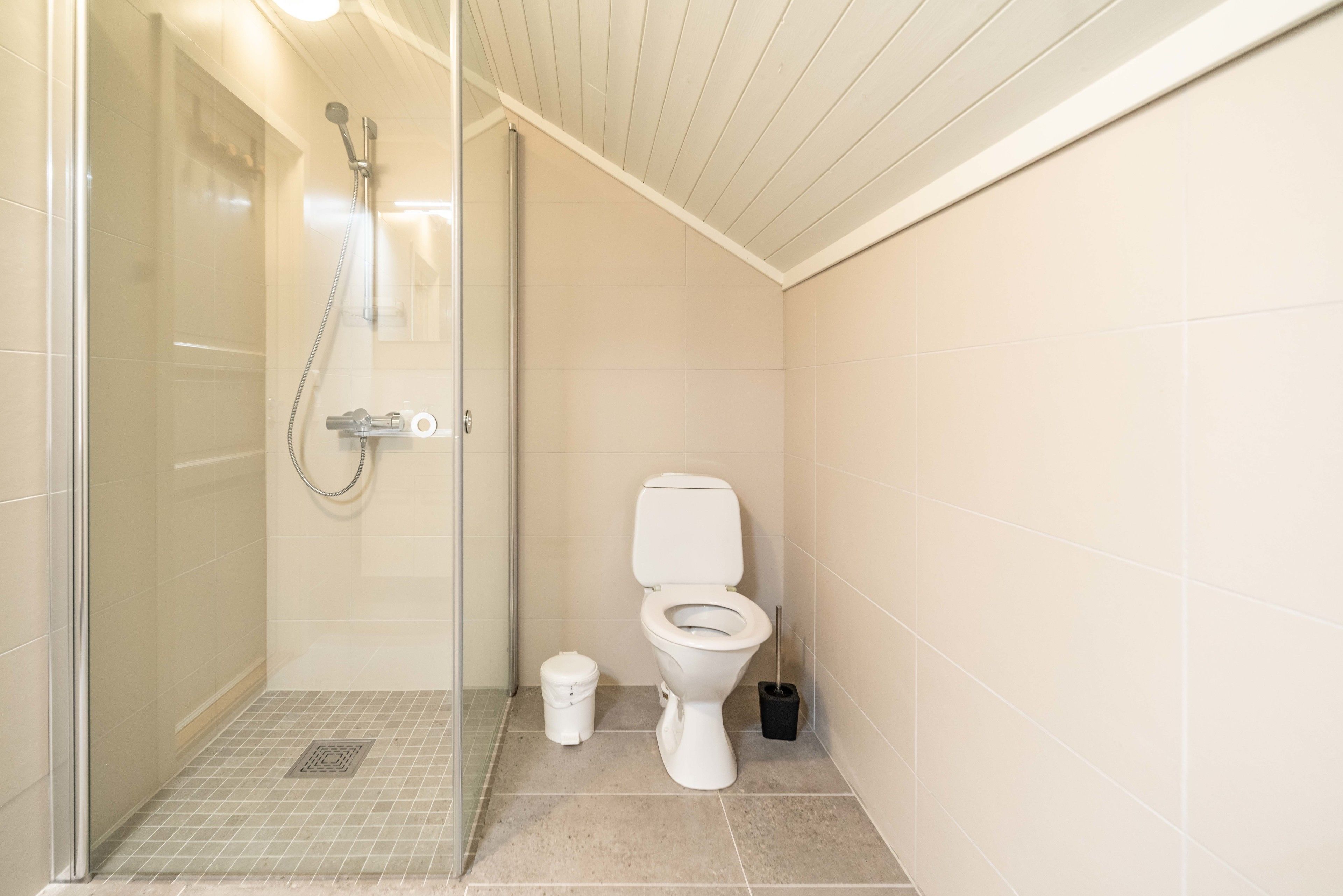 A small, clean bathroom with a toilet, a shower, and a trash bin.