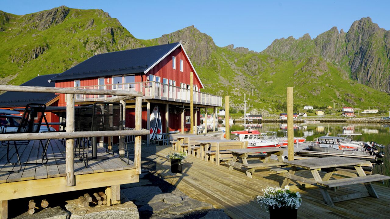 A wooden dock with a red building, boats, and mountains in the background.
