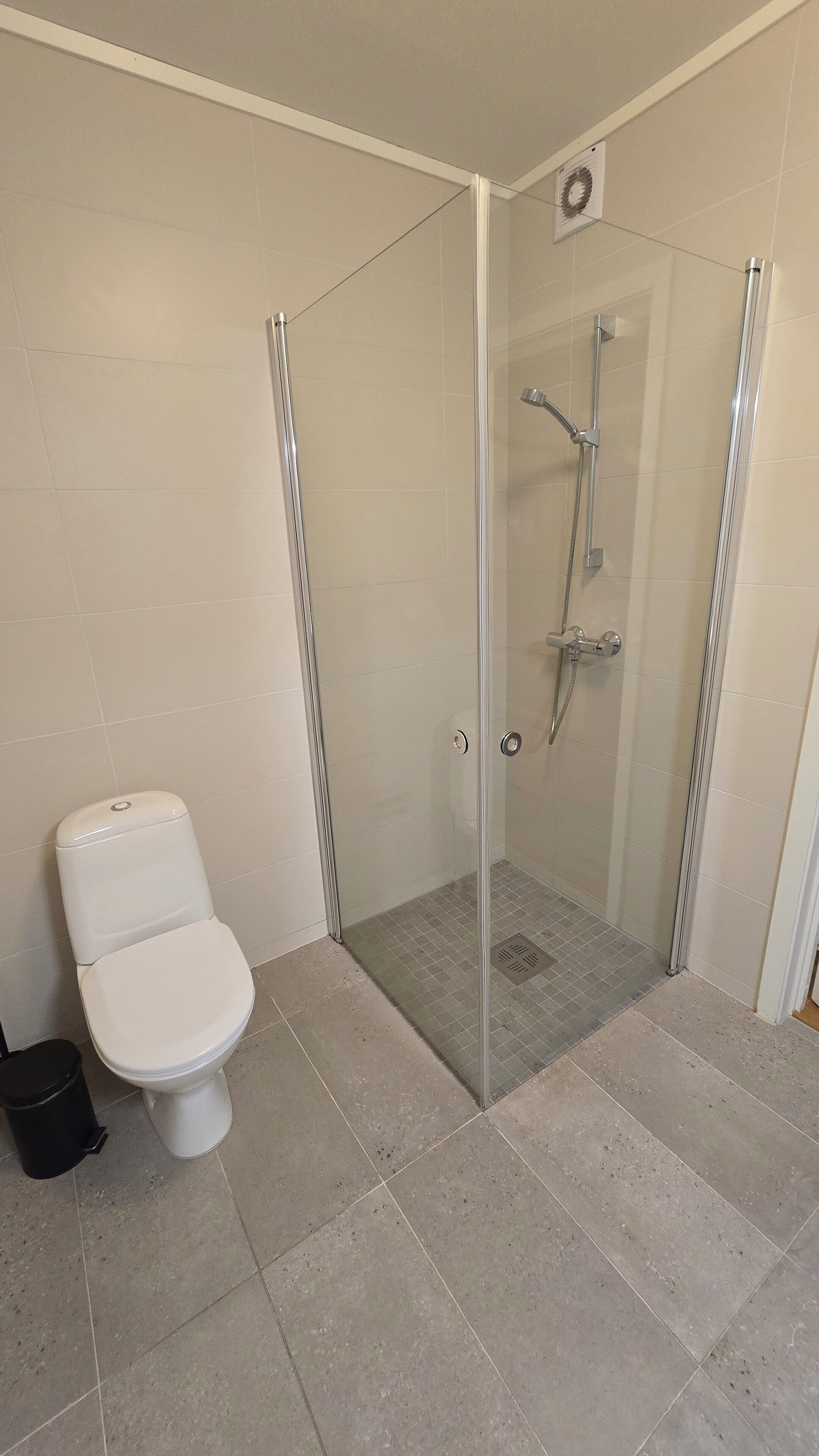 A bathroom with a toilet, a glass-enclosed shower area, and tiled flooring.