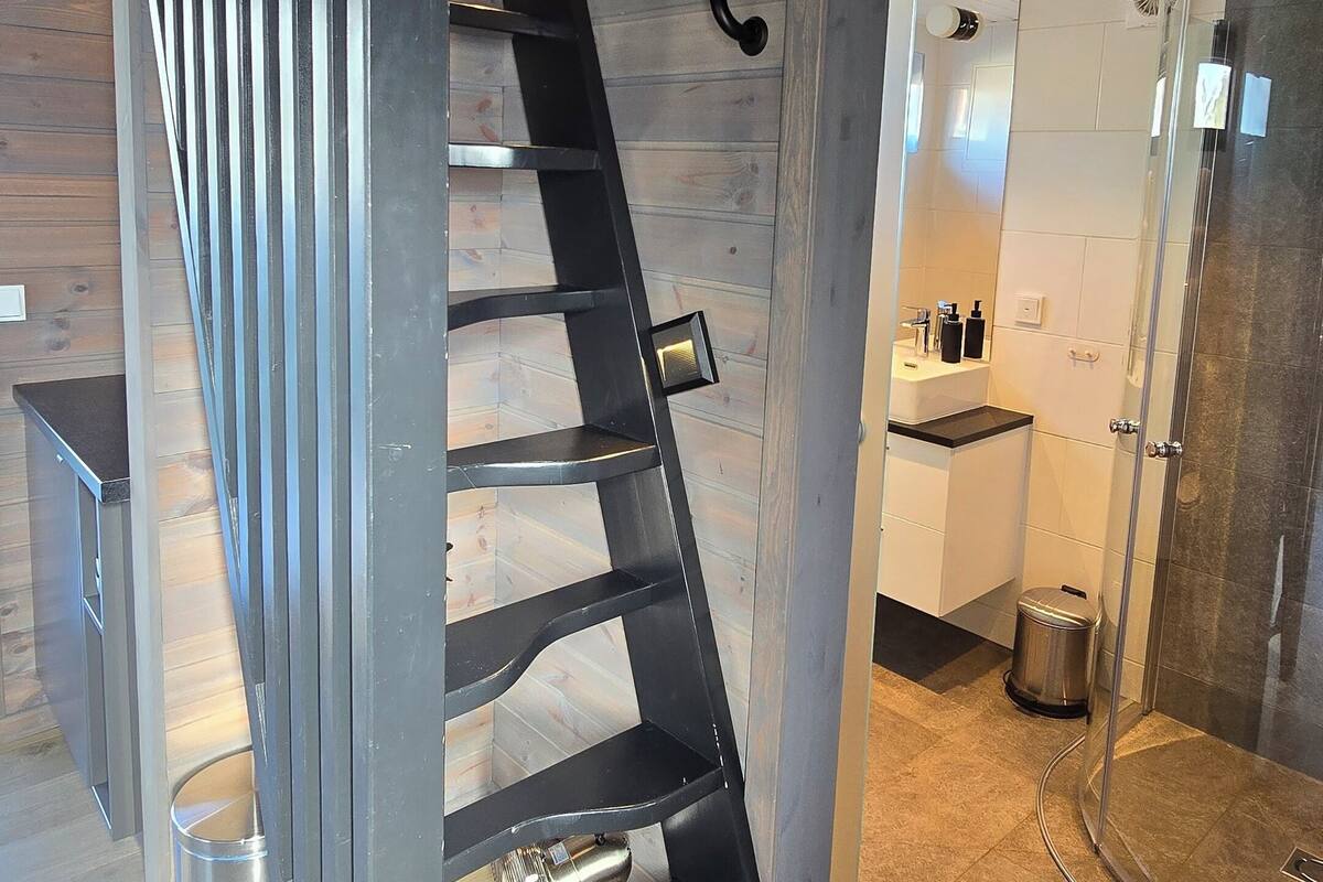A modern interior with a wooden staircase, a glass shower enclosure, and a kitchen area.
