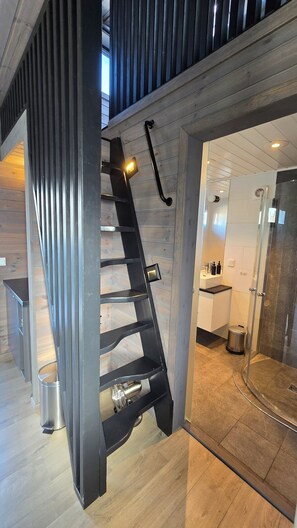A modern interior with a wooden staircase, a glass shower enclosure, and a kitchen area. - Hemmingodden Lodge (Vestvågøy)