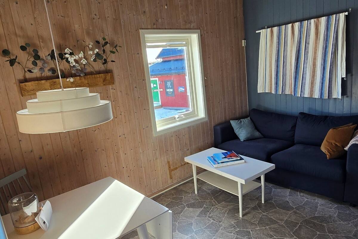 A cozy living area with a stone floor, a white table, a blue sofa, and a window with a view of a building outside.