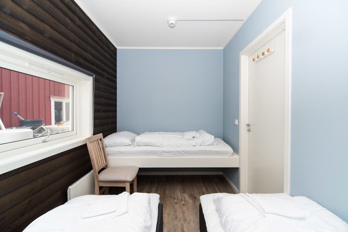 A small, single-room hotel room with a bed, a chair, a window, and a door.