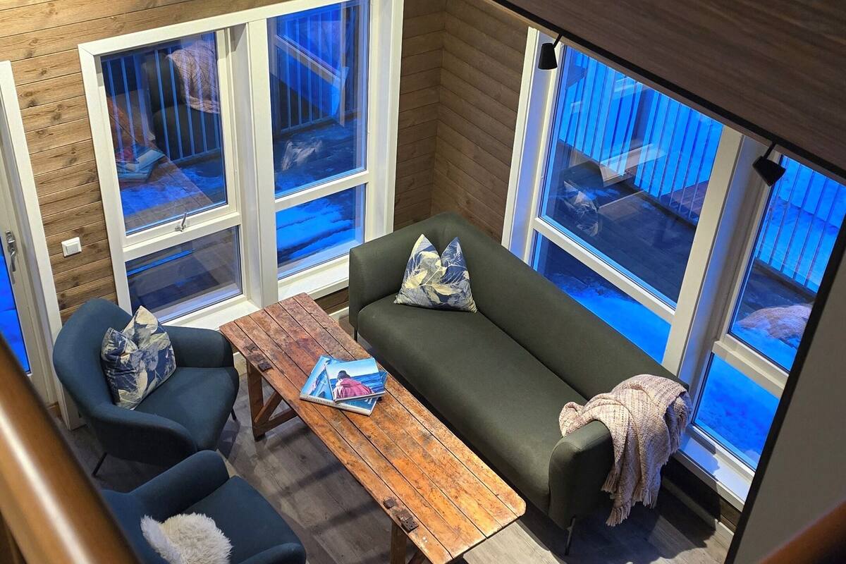 A modern interior with a wooden ceiling, a green sofa, blue armchairs, and a wooden coffee table.