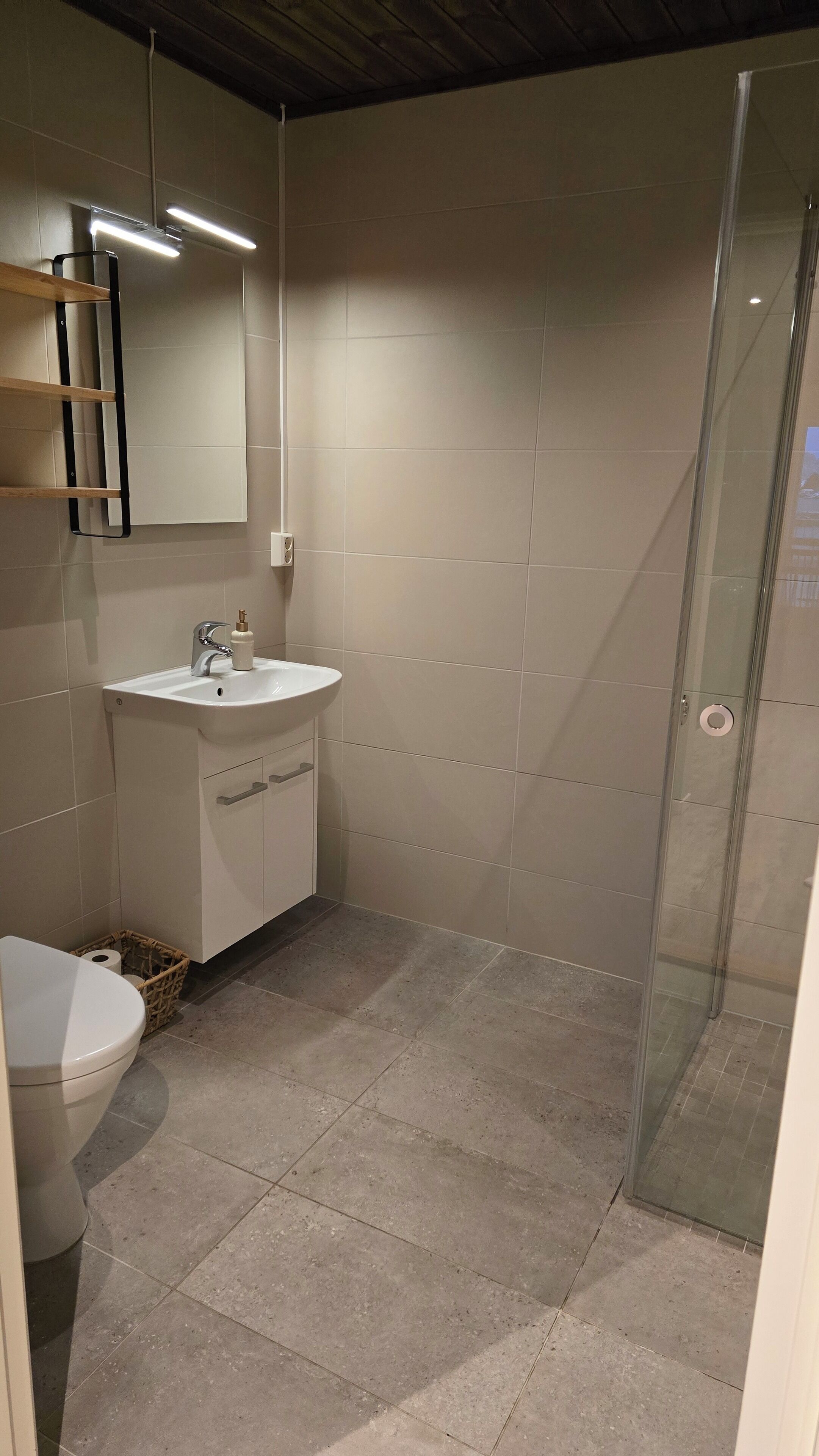A bathroom with a white sink, mirror, and toilet. There is a shower area with a glass door.