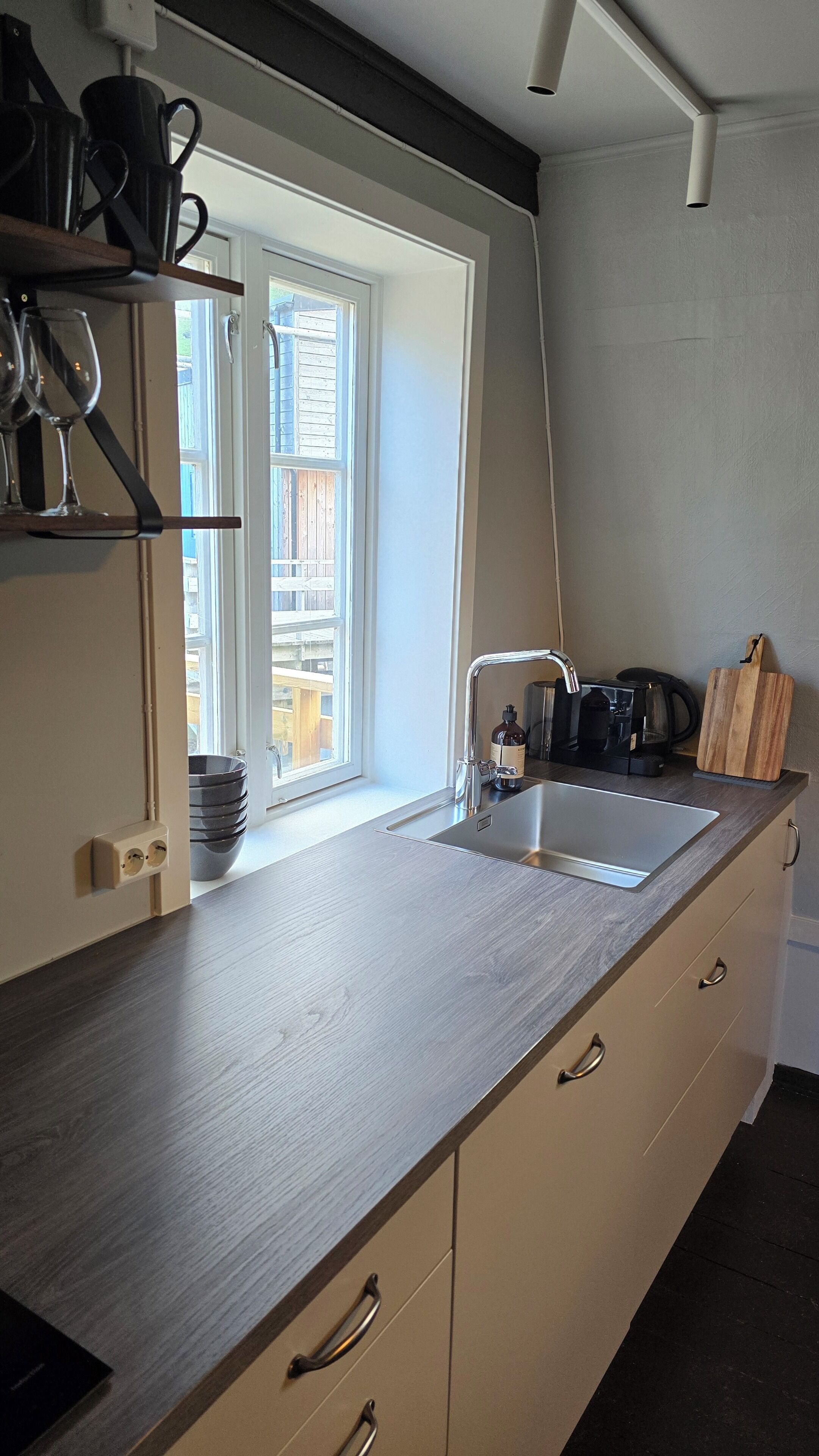 A kitchen with a window, a sink, a coffee maker, and a cutting board.