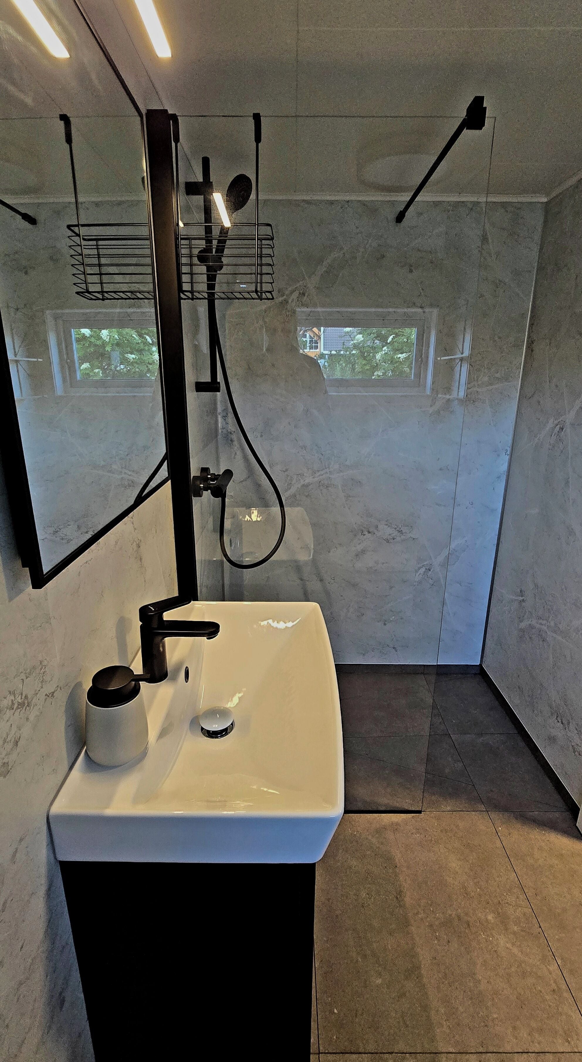 A modern bathroom with a white sink, black faucet, and a glass shower enclosure.