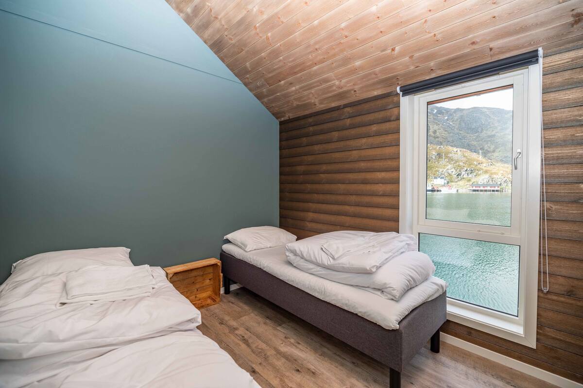A bedroom with a bed, a window with a view of a lake, wooden walls, and a sloped ceiling.