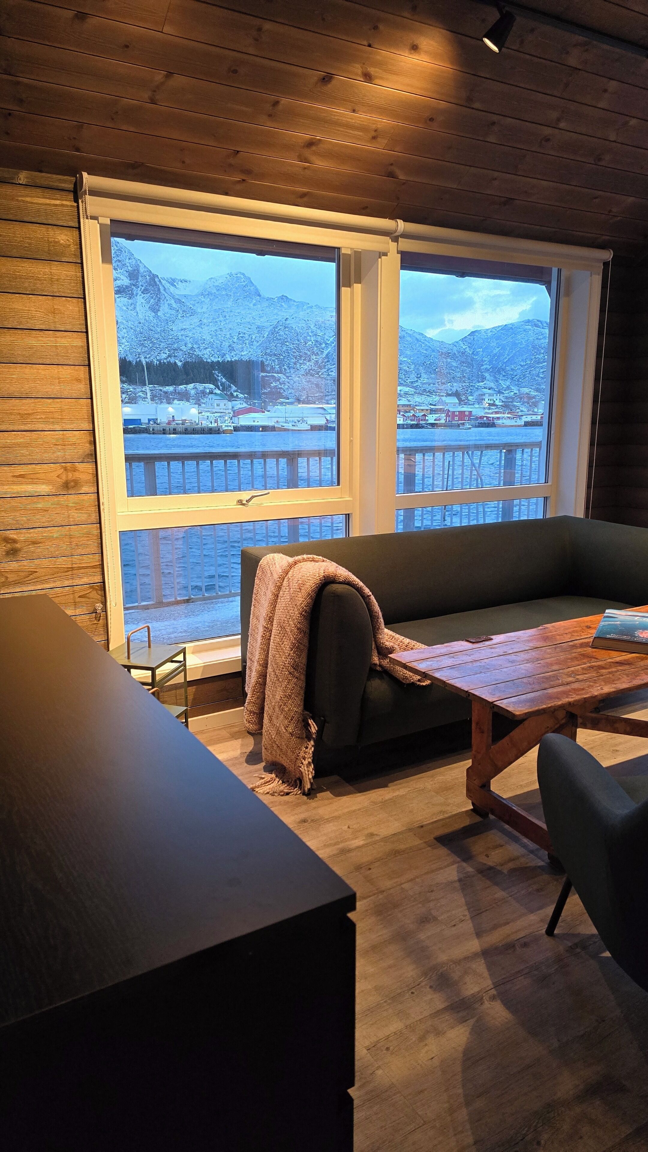 Una habitación acogedora con techo de madera, un sofá oscuro, una mesa de madera y vistas a un paisaje nevado a través de amplios ventanales.
