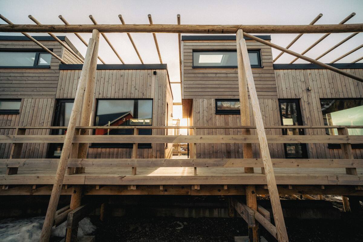 A modern building with wooden exterior panels, multiple windows, and a wooden staircase leading to an upper level.
