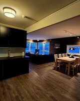 Una cocina moderna con armarios oscuros, una mesa de comedor de madera y un ventanal con vista a un estacionamiento.