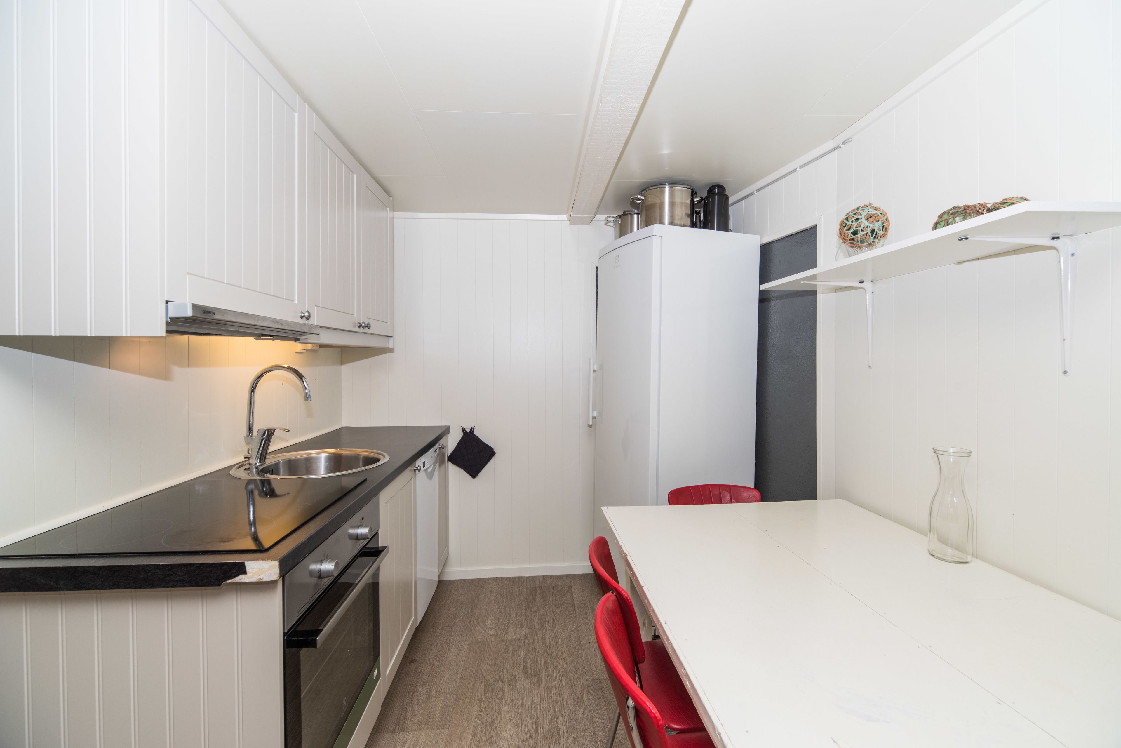 Une cuisine compacte avec des meubles blancs, un plan de travail noir et un petit coin repas doté de chaises rouges.