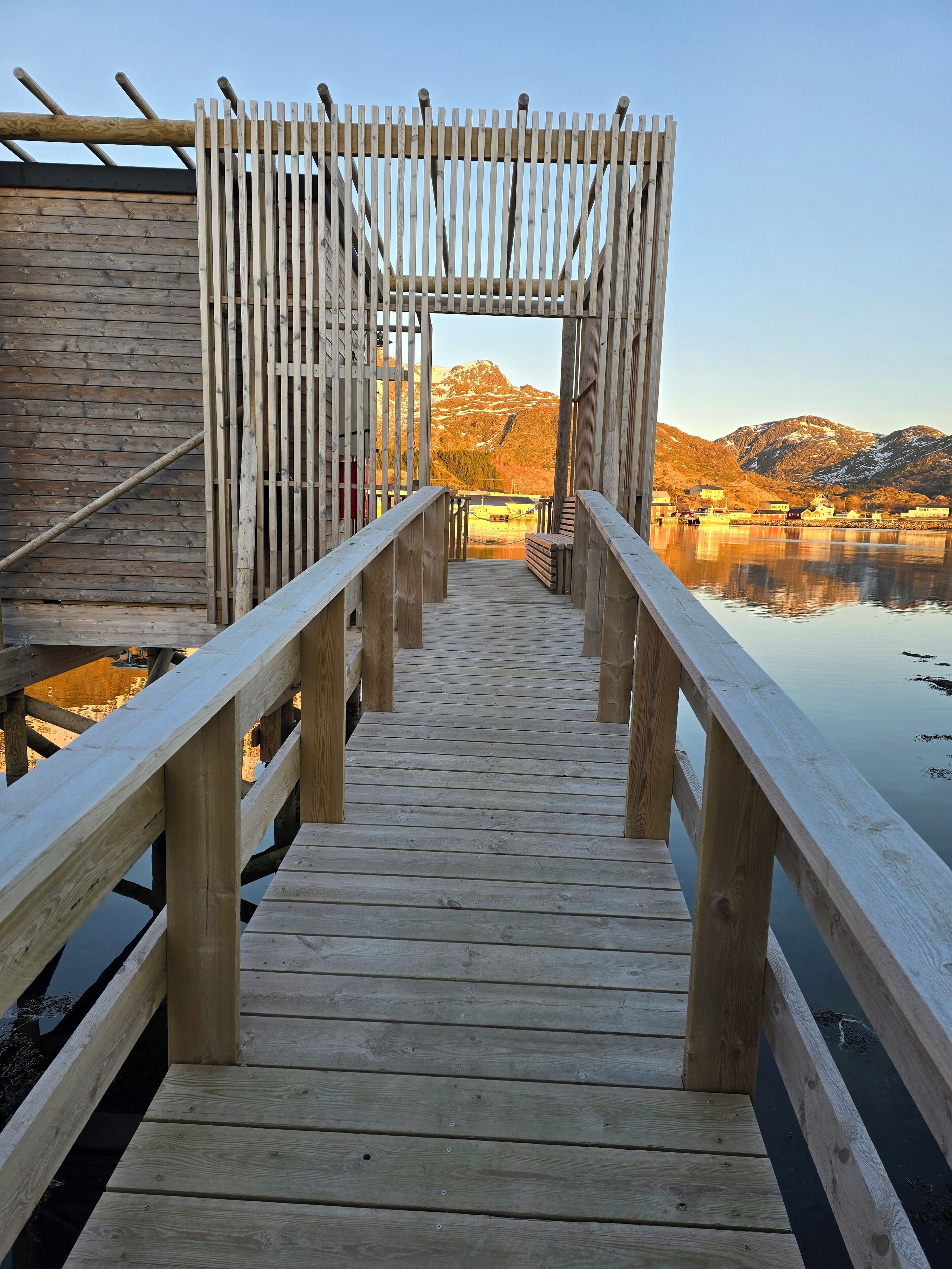 A wooden pier leading to a wooden structure with a view of mountains and a lake.