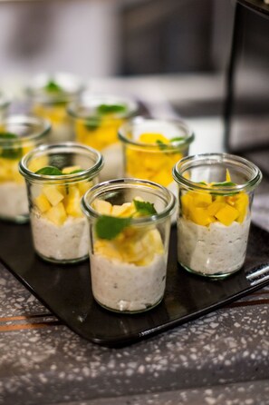 A tray of small glass containers filled with a layered dessert, possibly pudding or mousse, with mango pieces and mint leaves on top.