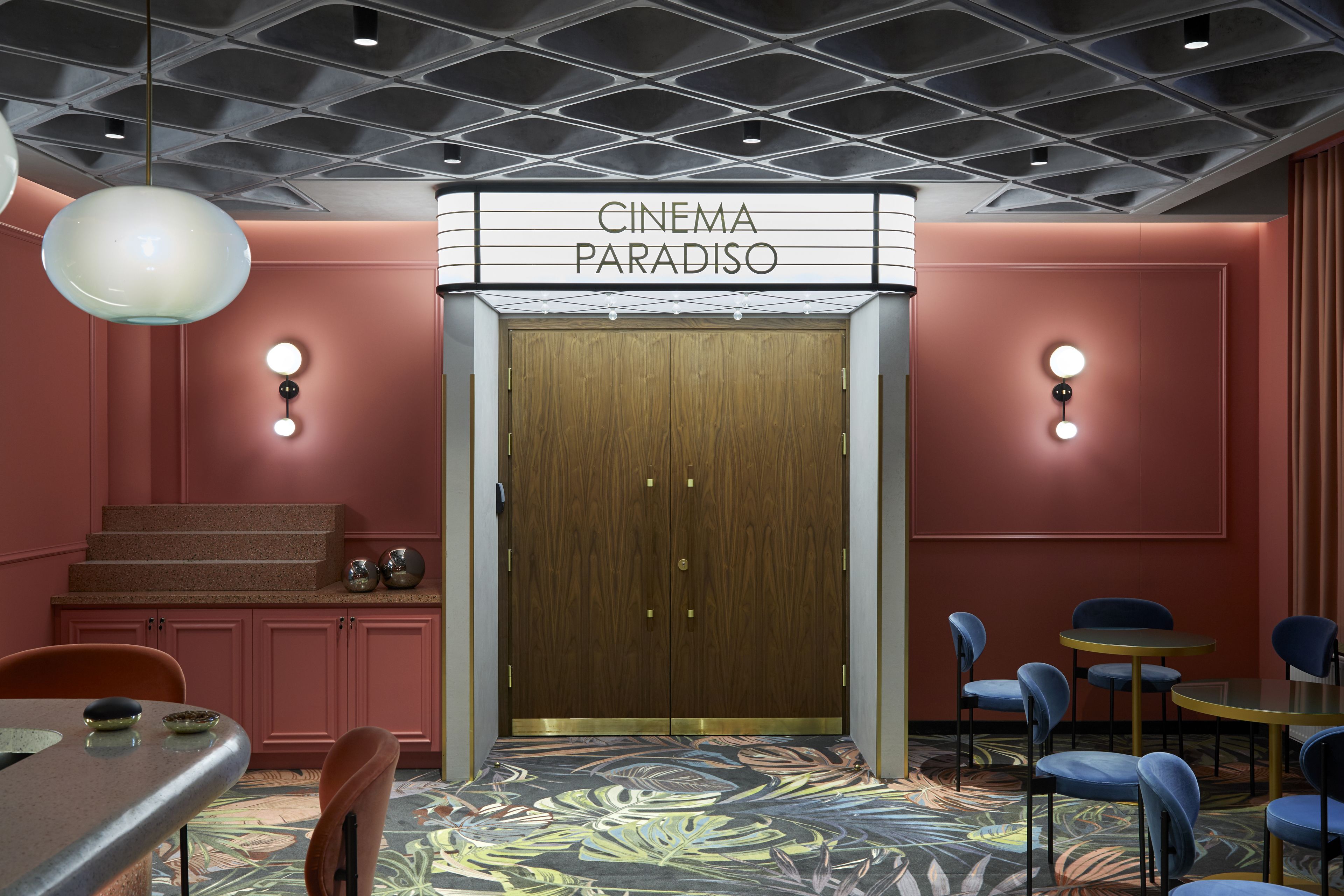 Un cine con una puerta de madera y un cartel encima. Hay sillas y mesas alrededor.