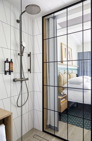 A modern hotel room with a shower, a bed, a bedside table, and a bathroom with a toilet.