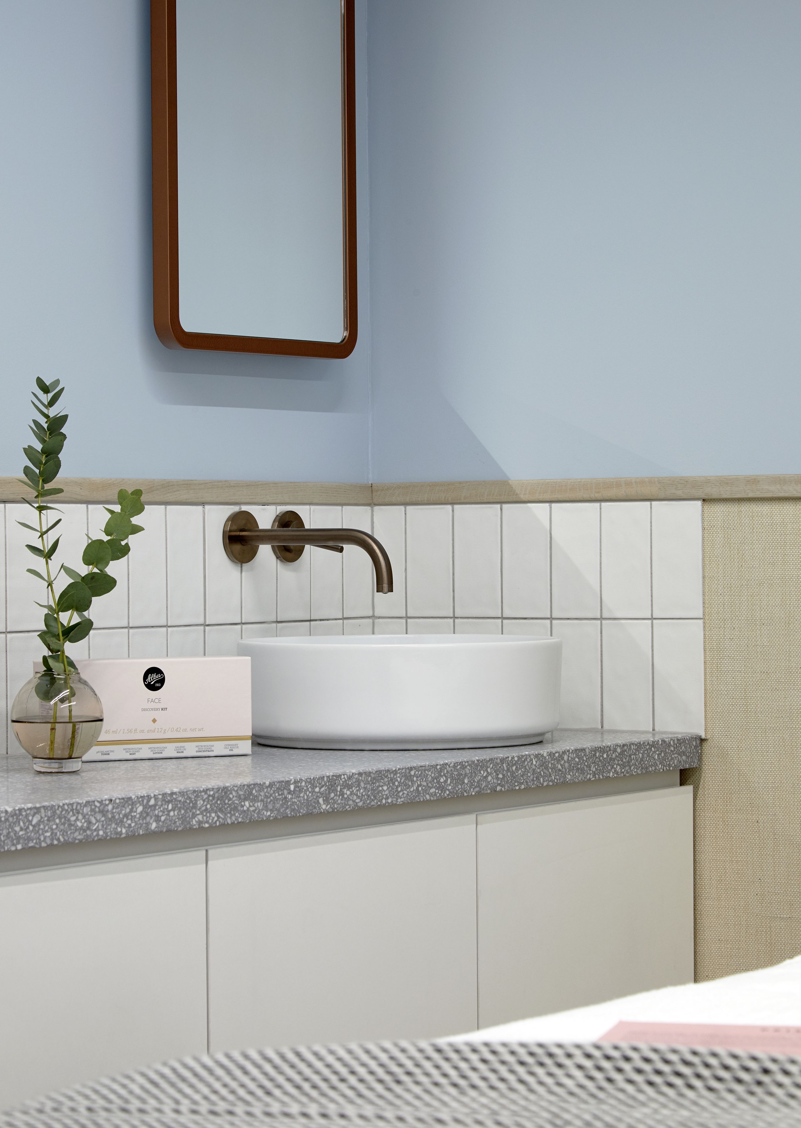 Een badkamer met een witte wastafel, een spiegel en een plant op het aanrecht.