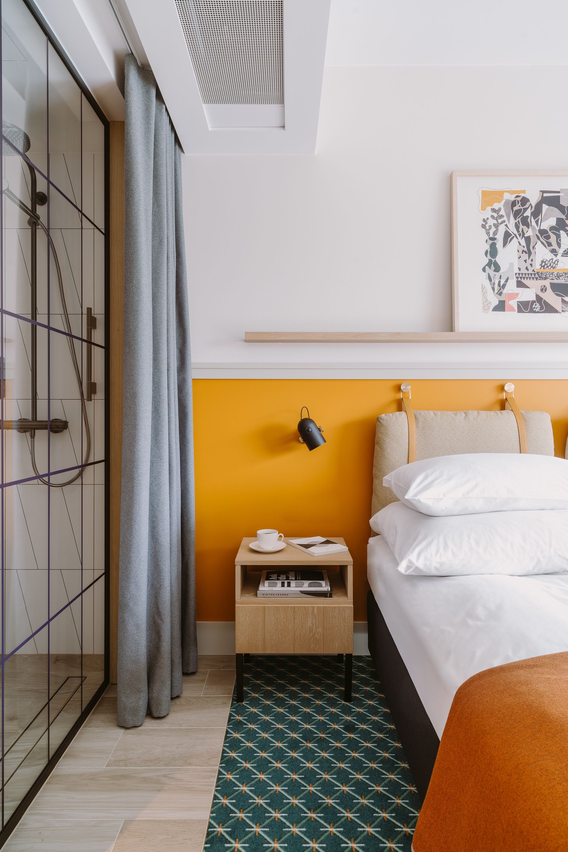 A hotel room with a bed, a nightstand, a lamp, a wardrobe, and a patterned rug.
