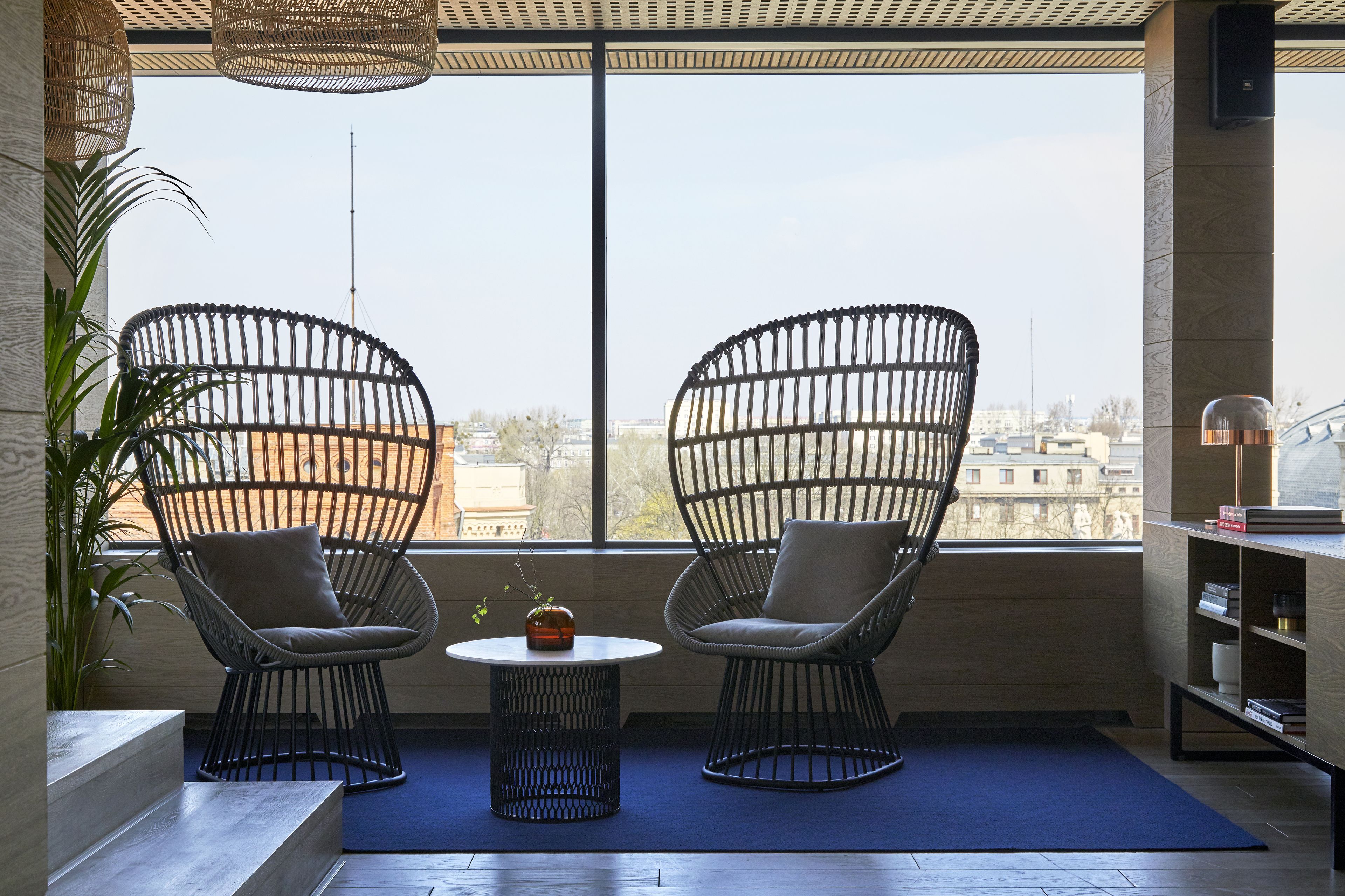 Una habitación moderna con dos sillones de mimbre negro, una mesita redonda y una estantería.