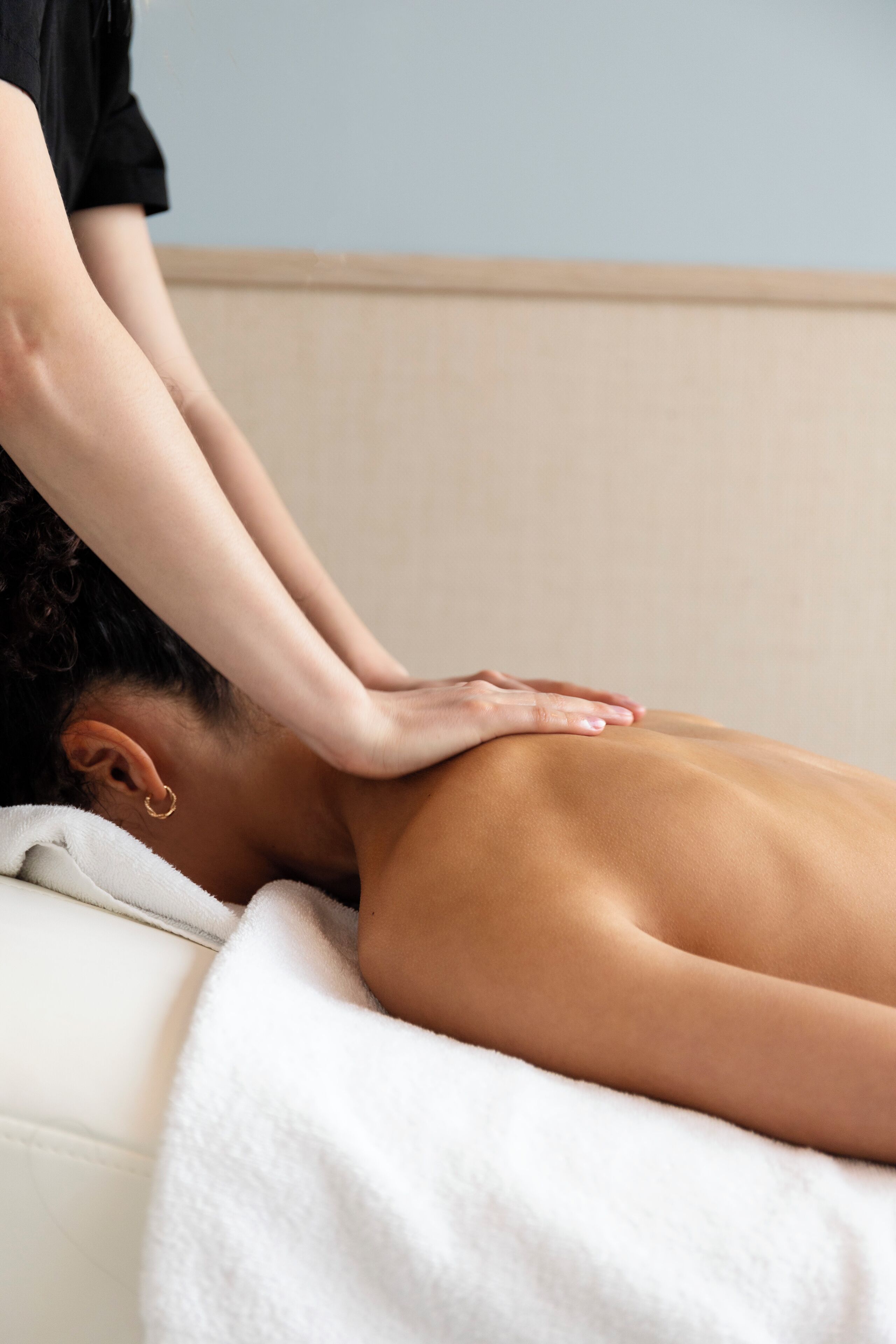 A person receiving a back massage on a white massage table with a beige wall in the background.