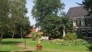 Un jardin bien entretenu, avec un chemin qui mène à un bâtiment à la façade en briques et aux volets verts.