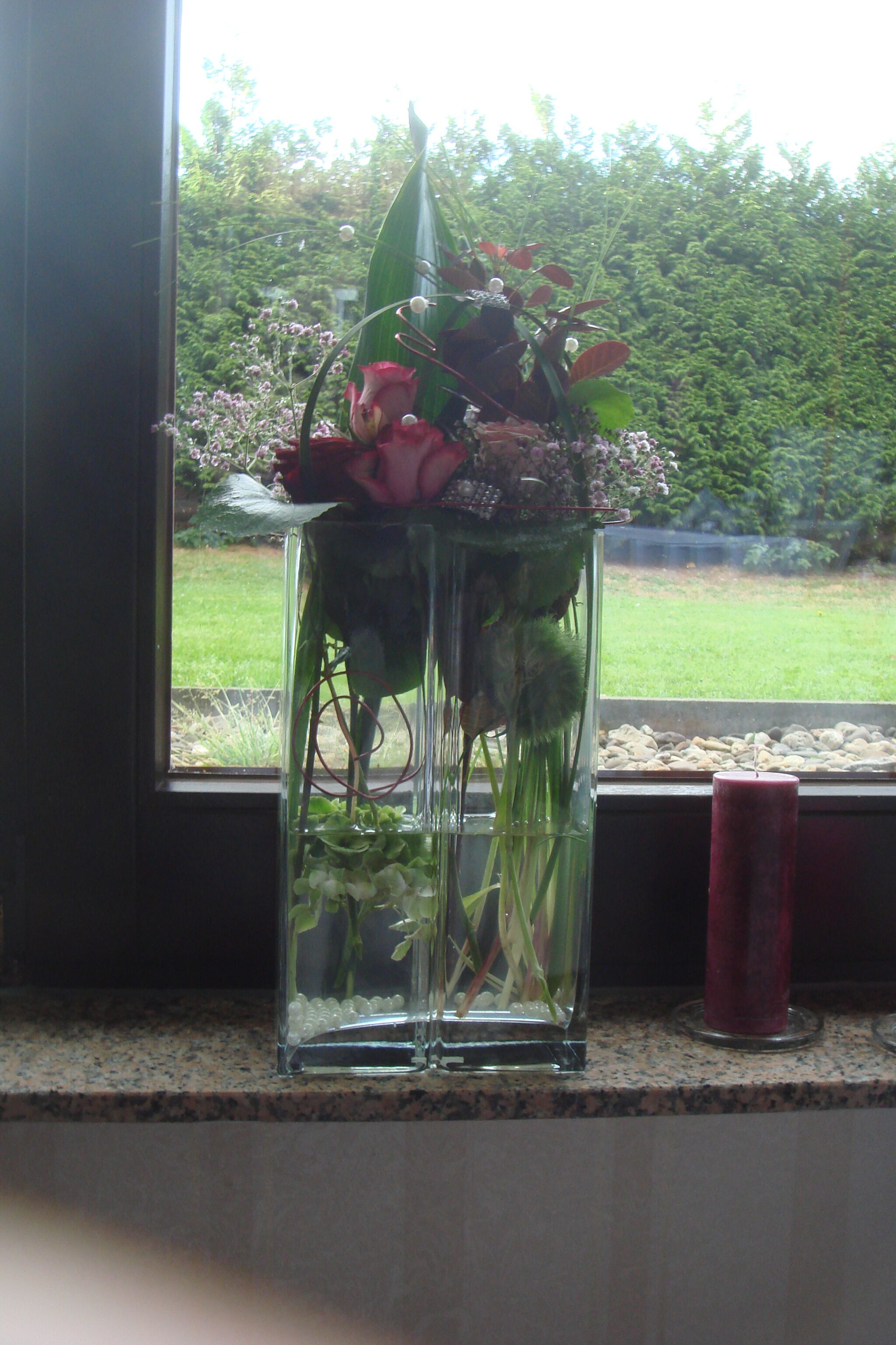 A clear glass vase with flowers on a windowsill.