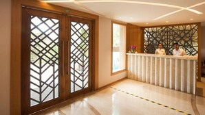 Zona de recepción de hotel con un diseño moderno, que incluye un mostrador de recepción, dos recepcionistas y un ventanal con vistas a zonas verdes.