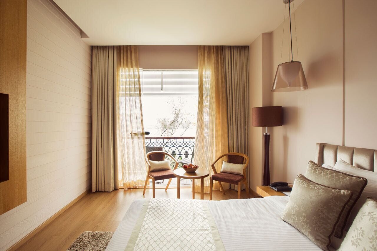 Et hotelværelse med en seng, to stole, et lille bord, en lampe og udsigt ud.