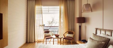 A hotel room with a bed, two chairs, a small table, a lamp, and a view of the outside.