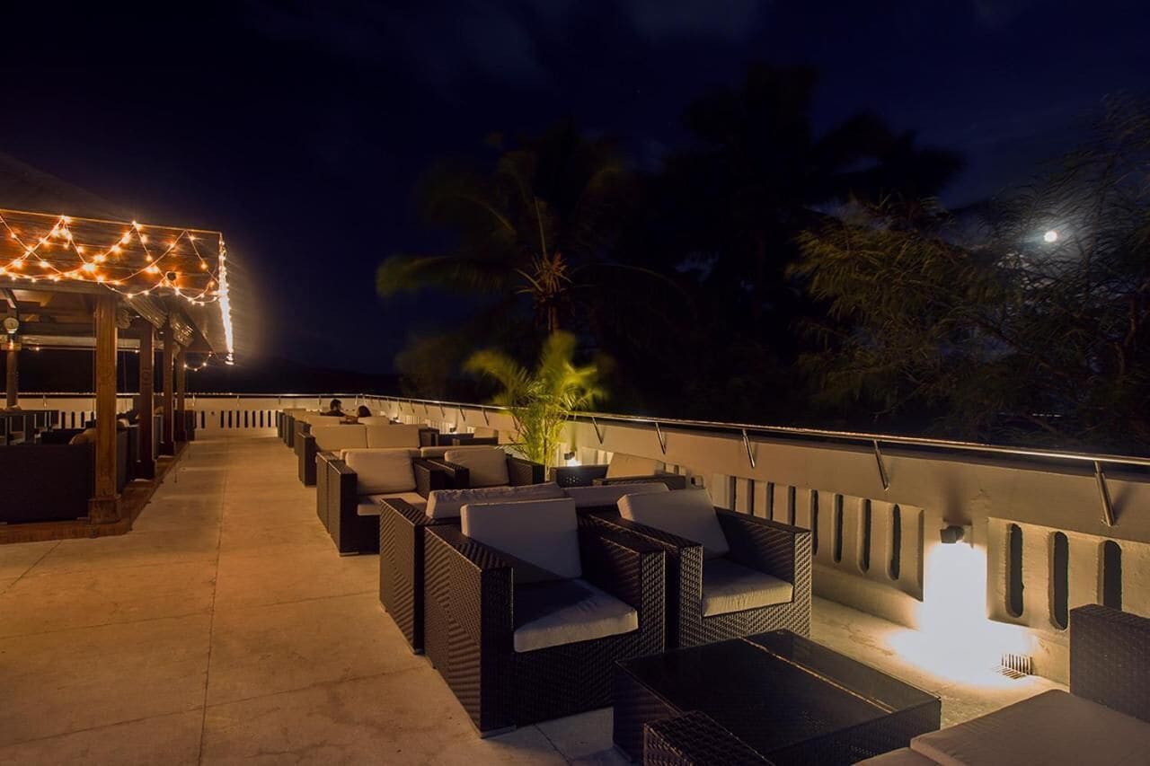 An outdoor seating area with wicker furniture and string lights, overlooking a body of water.