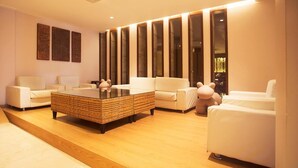Una sala de estar moderna con una mesa de centro de vidrio, sofás blancos y un amplio ventanal con persianas verticales.