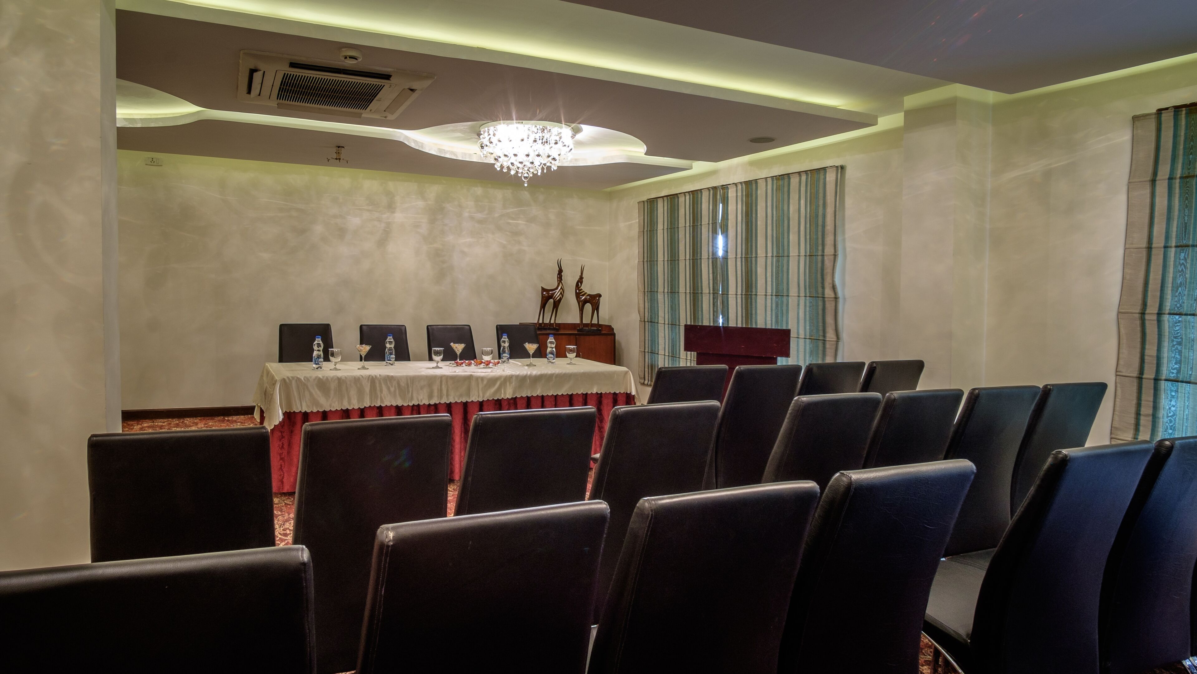 A conference room with a long table, chairs, a chandelier, and a podium.