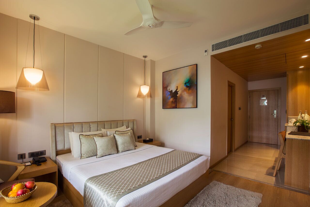 Hotelkamer met een groot bed, twee bedlampen, een plafondventilator, een schilderij aan de muur en een tafeltje met fruit.