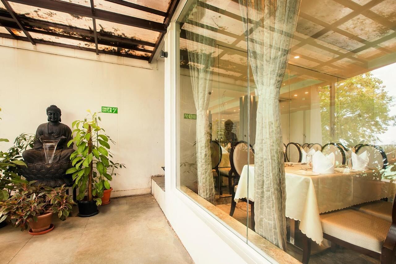 Un espacio interior tranquilo con una estatua de Buda, plantas en macetas y un comedor con mesa y sillas.