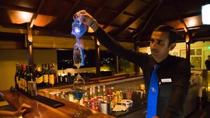 Un cantinero sirviendo una bebida en una barra con varias botellas y vasos.