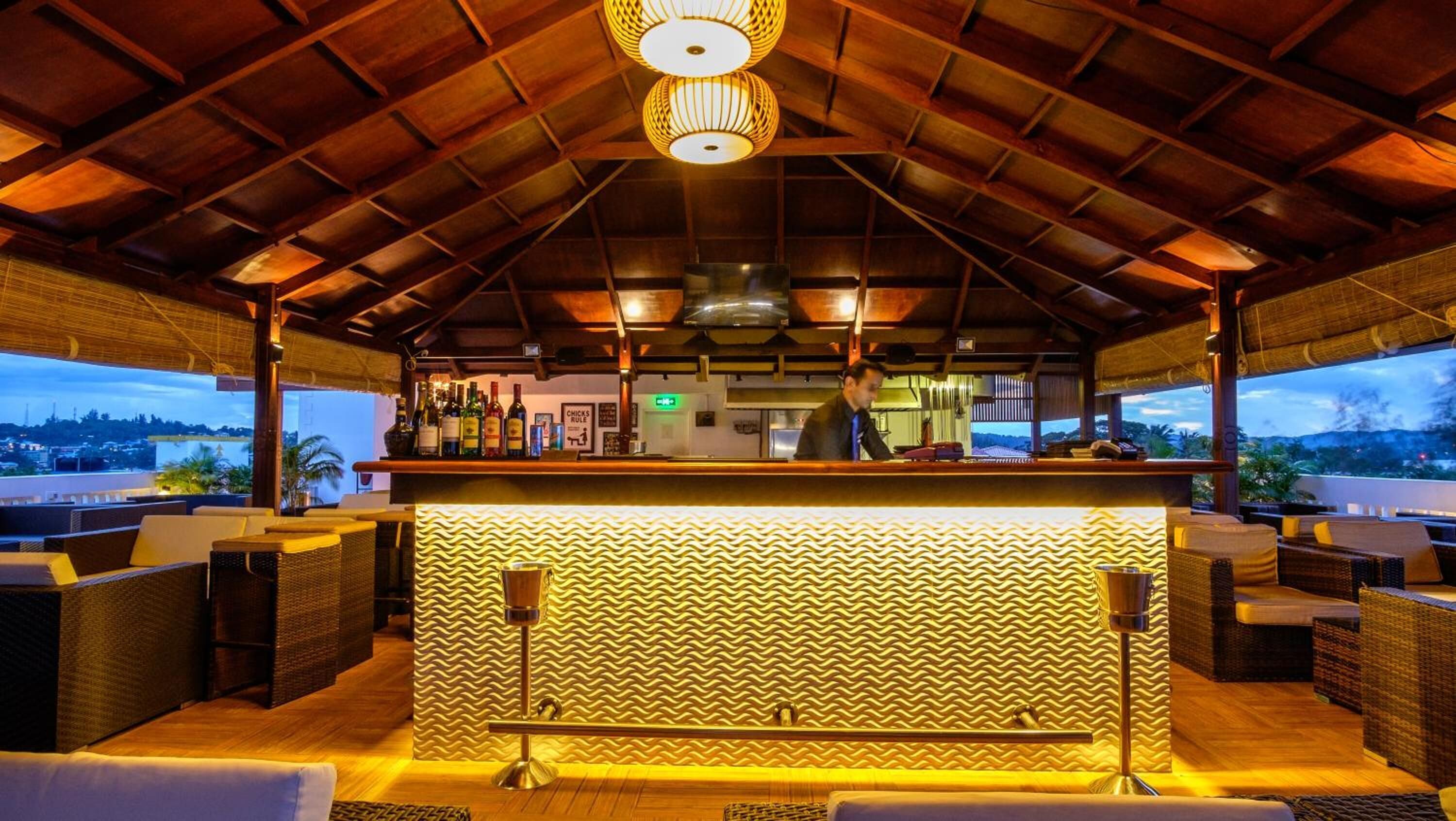 Een bar met rieten meubilair, een patroonmuur en uitzicht op de stad.