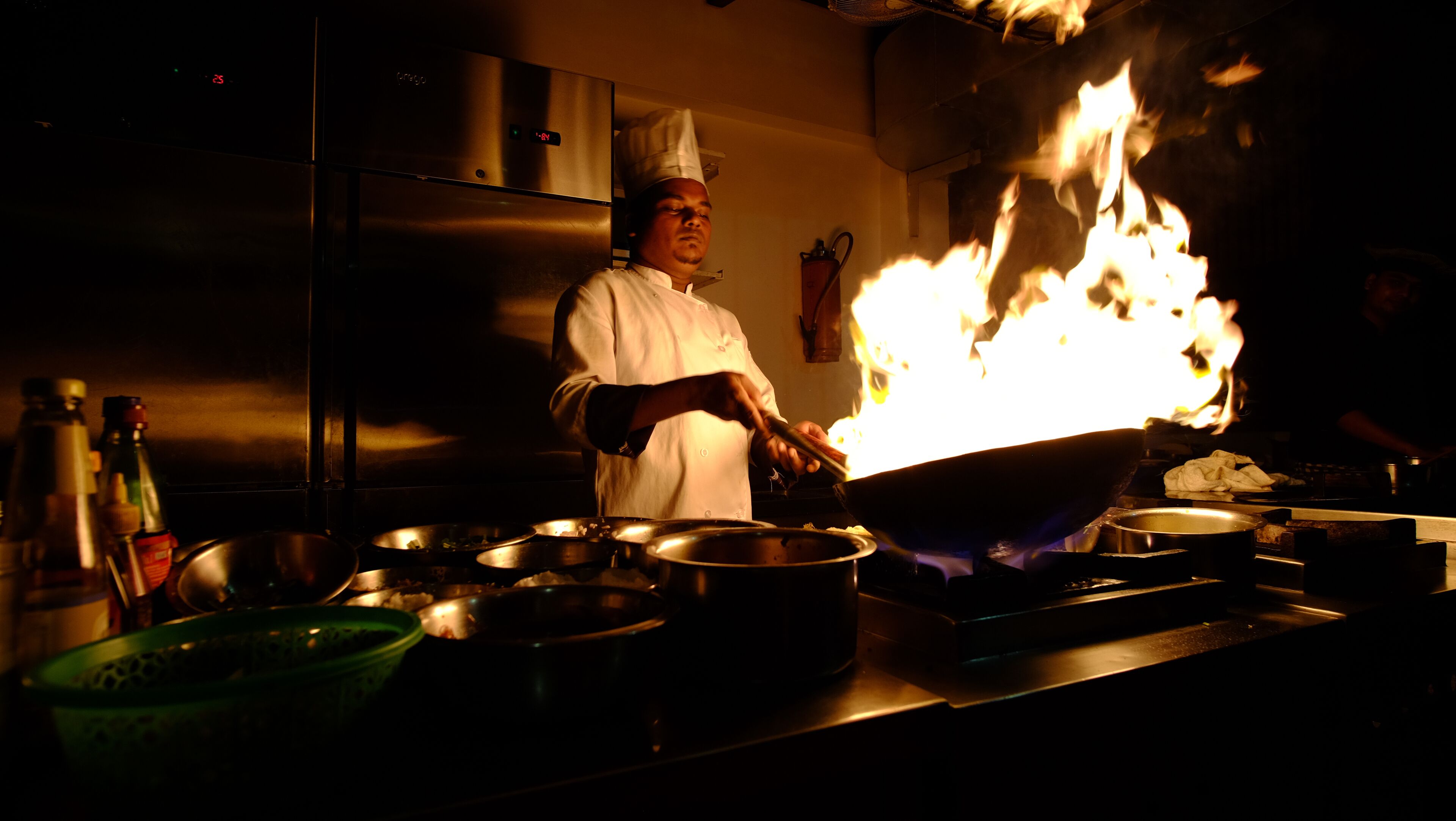 A chef cooking with a large wok over an open flame in a kitchen.
