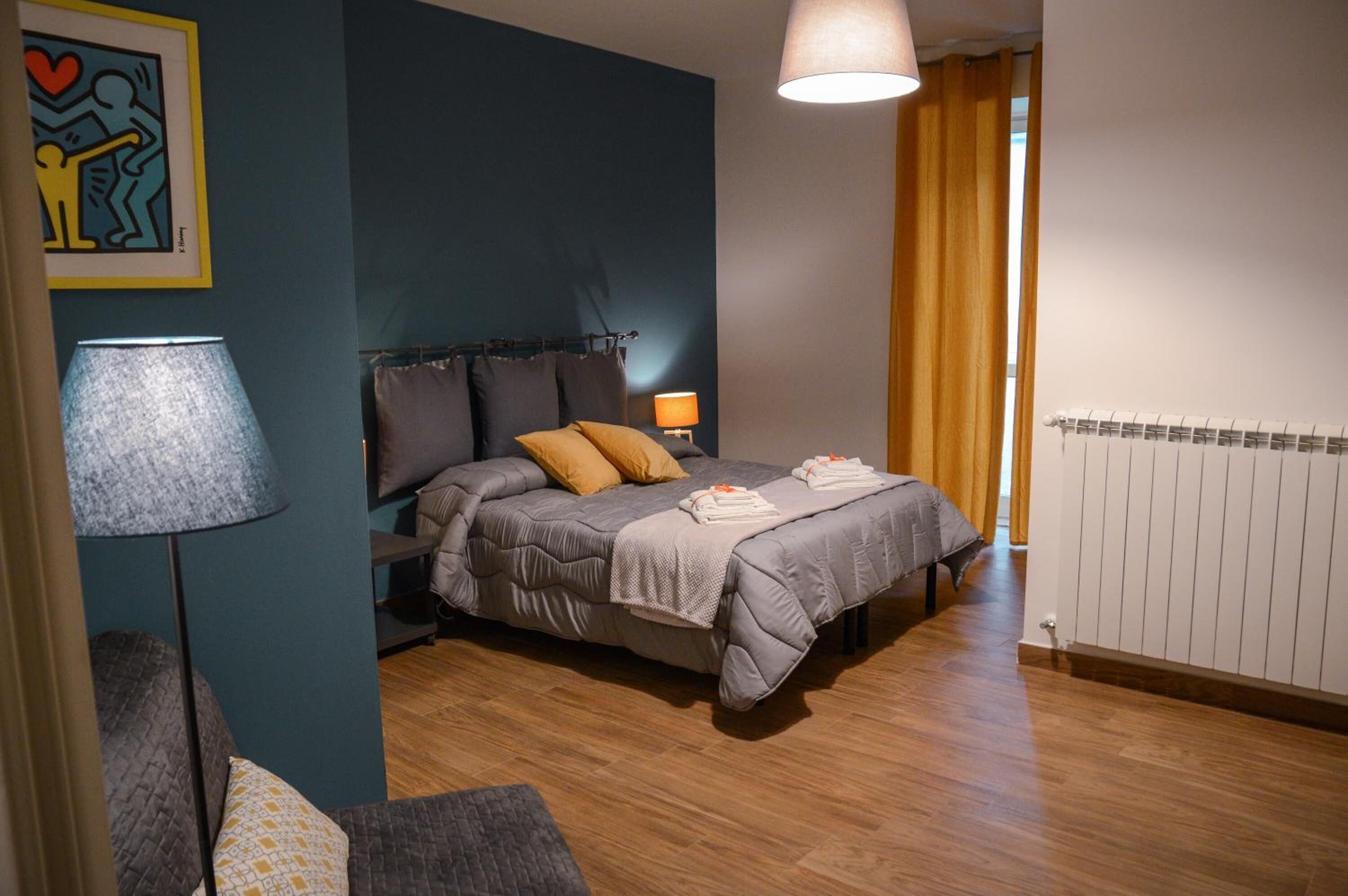 Ein Schlafzimmer mit einem Bett, zwei Nachttischlampen, einem Heizkörper und einem Fenster mit Vorhängen.