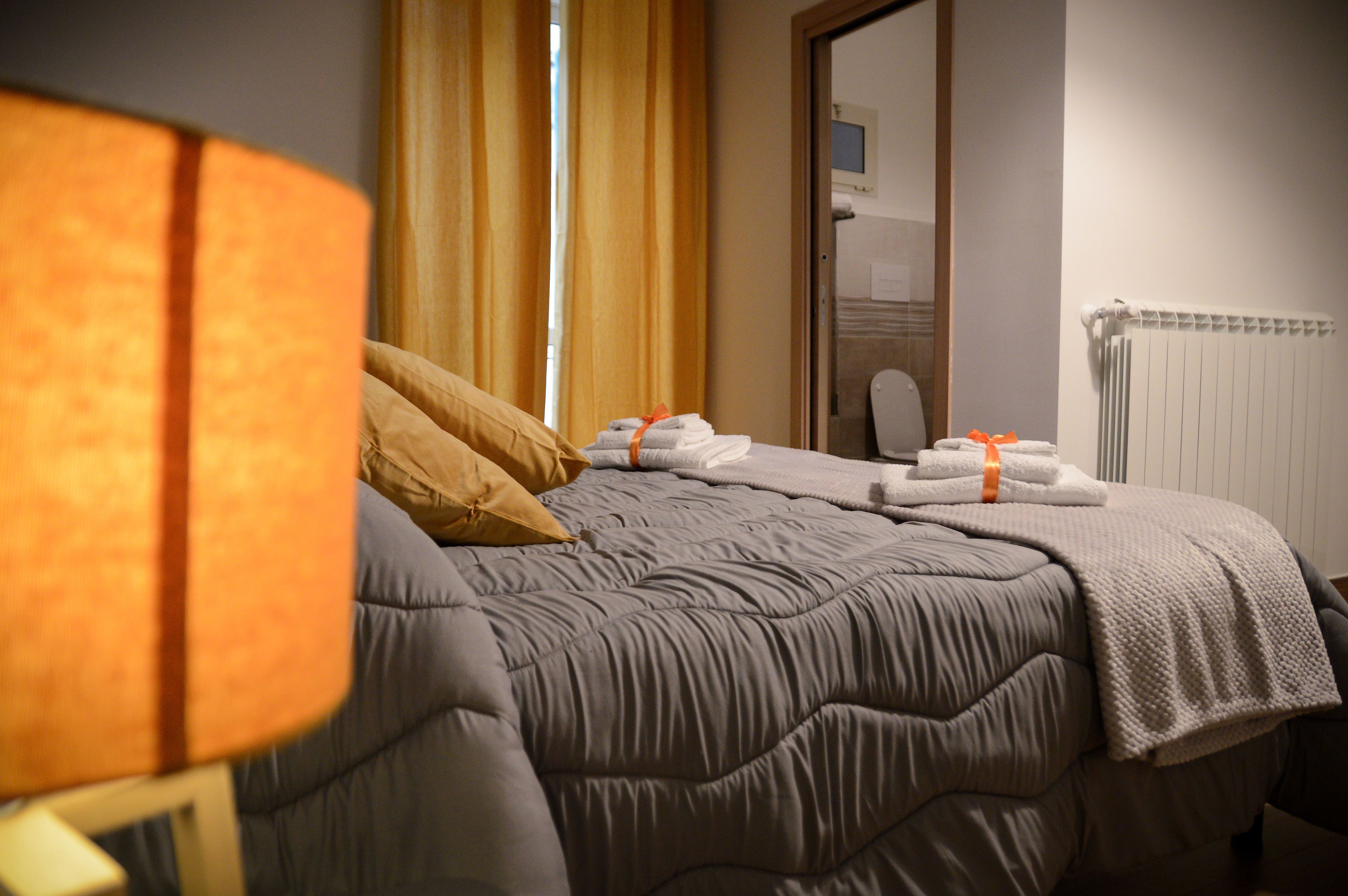 Habitación de hotel con cama, ventana con cortinas, radiador y espejo en la pared.