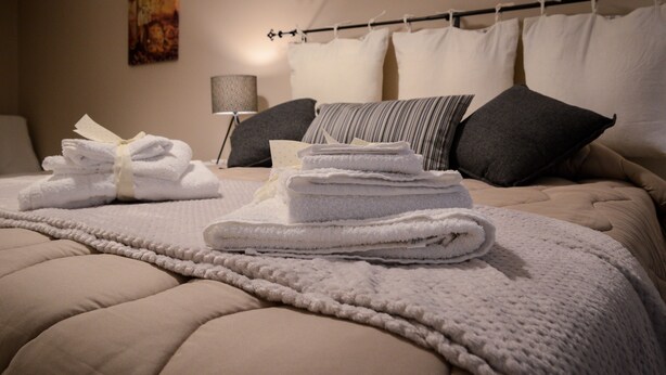 A neatly made bed with a beige comforter, white towels, and a striped pillow. - La Fara B&B (Benevento)