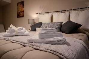 Un lit bien fait, avec une couette beige, des serviettes blanches et un oreiller à rayures.